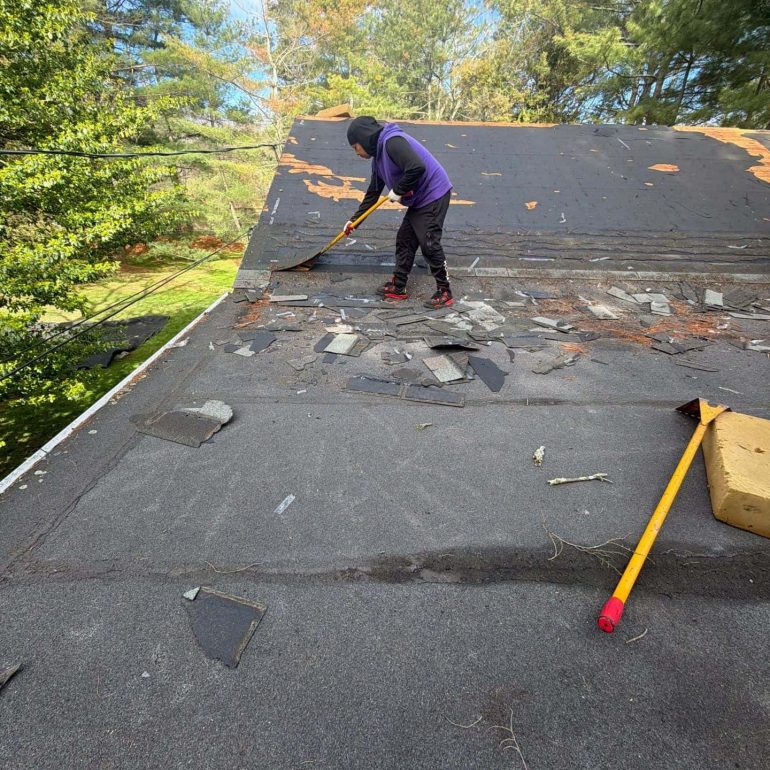 Worker removing old shingles during a residential roof replacement project to prepare for new roofing installation