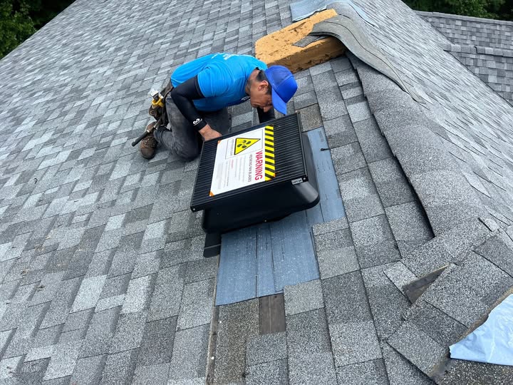 A professional worker installing a roof ventilation system on a residential shingle roof, ensuring proper airflow and attic ventilation.