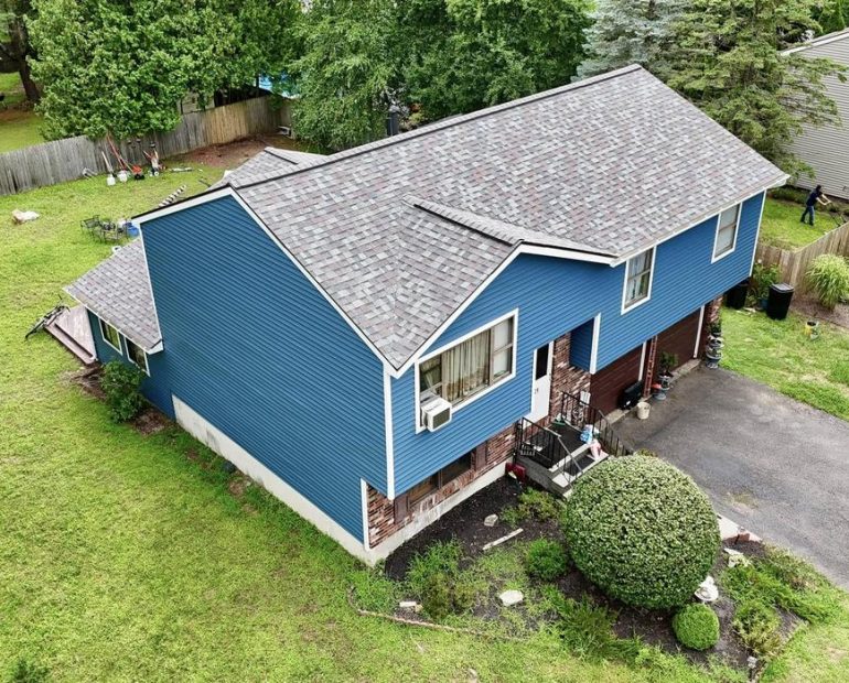 Aerial view of a blue two-story residential house with asphalt shingle roofing and a driveway