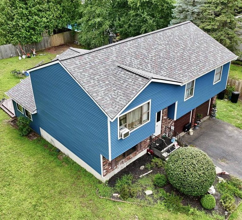 Aerial view of a blue two-story residential house with asphalt shingle roofing and a driveway