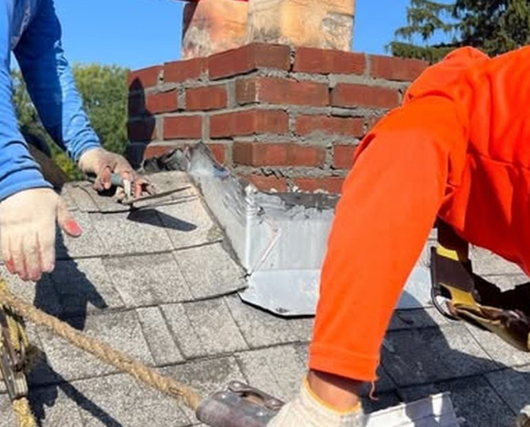 Roof replacement work near chimney showing damaged shingles and flashing