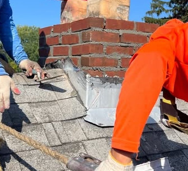 Roof replacement work near chimney showing damaged shingles and flashing