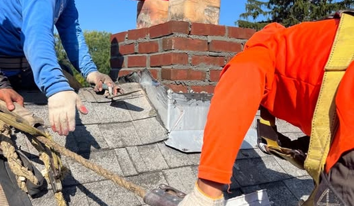 Roof replacement work near chimney showing damaged shingles and flashing