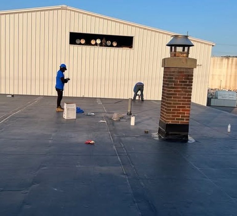 Professional roof leak repair on commercial flat roof with technicians sealing membrane and flashing