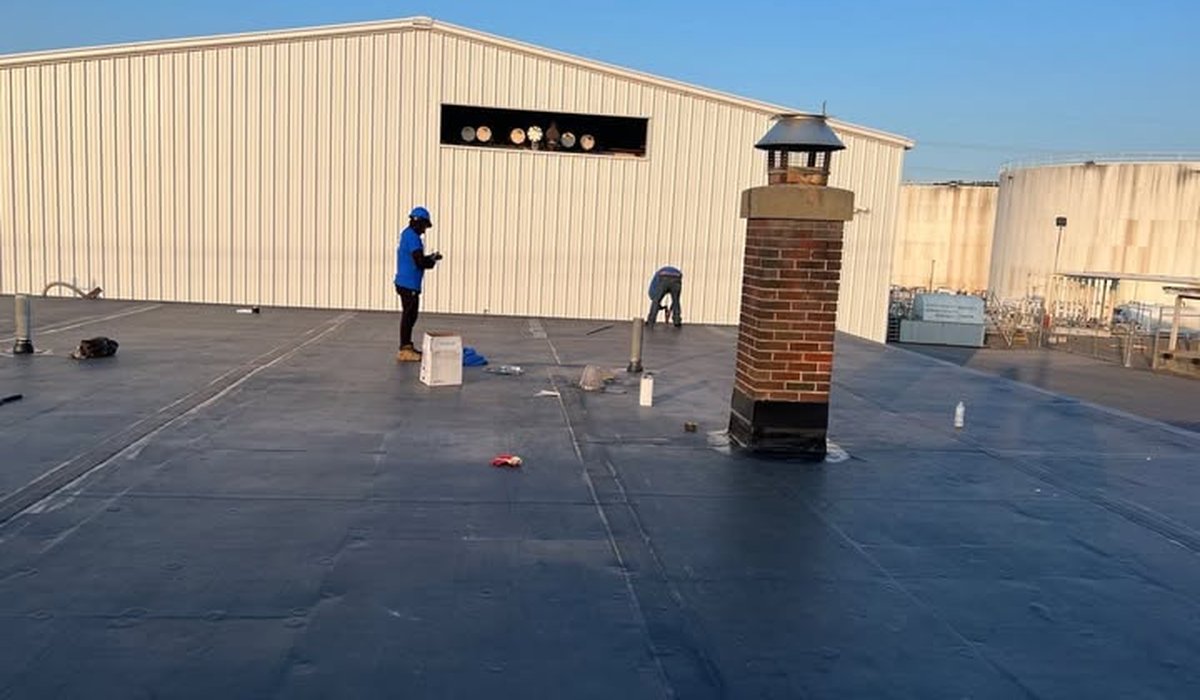 Professional roof leak repair on commercial flat roof with technicians sealing membrane and flashing