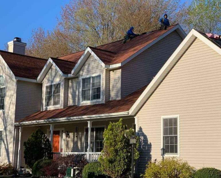 Residential roof replacement project showing professional roofers installing new asphalt shingles on house roof