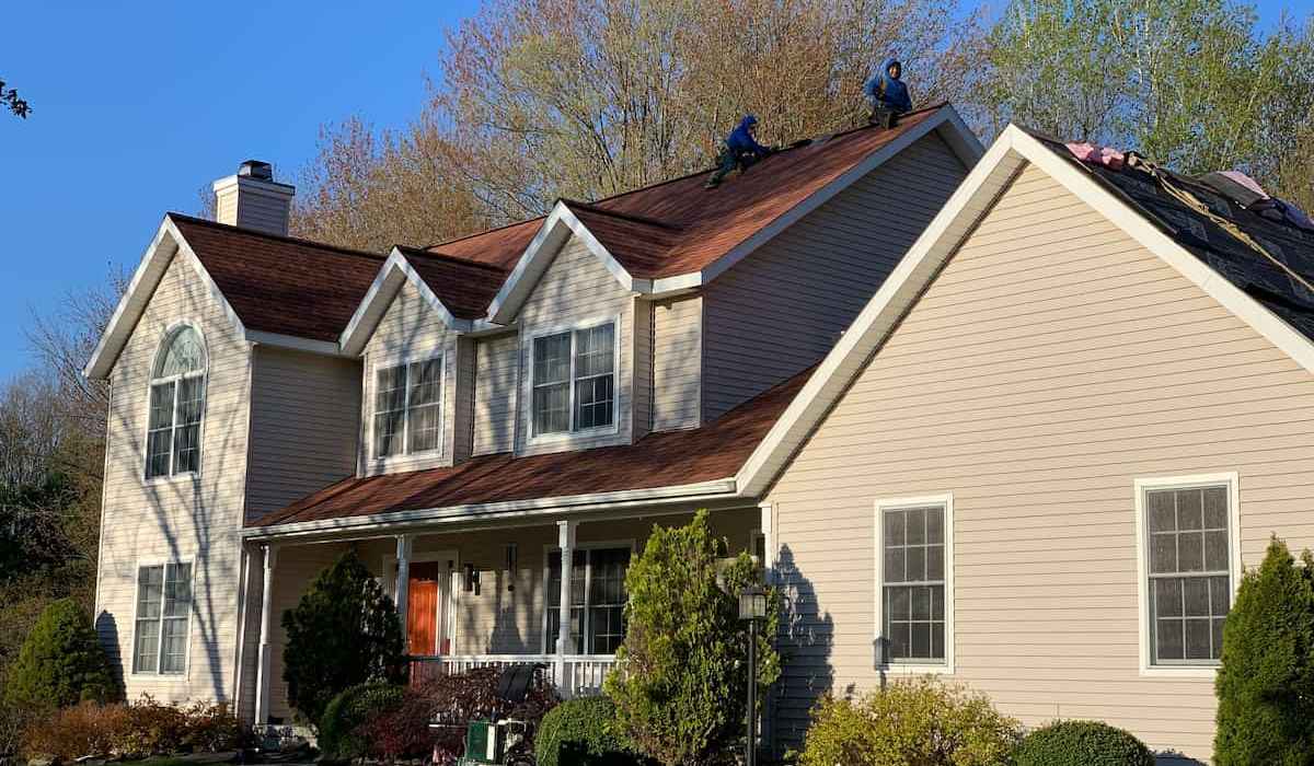 Residential roof replacement project showing professional roofers installing new asphalt shingles on house roof