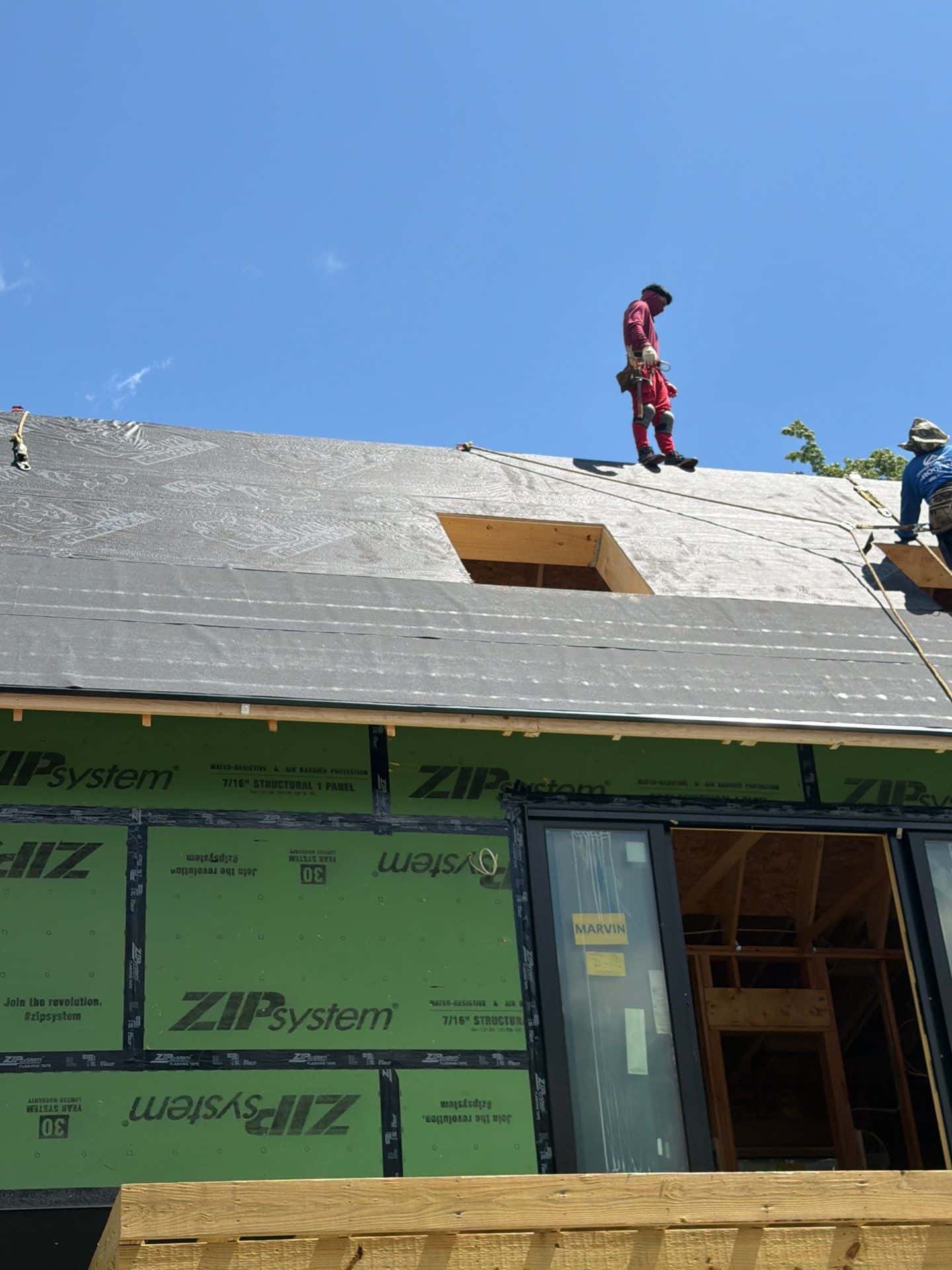 Professional roofers installing synthetic roofing underlayment over ZIP System roof sheathing before asphalt shingles on a new residential home.
