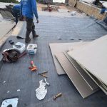 Commercial flat roof membrane preparation with workers installing roofing material over an exposed roof surface