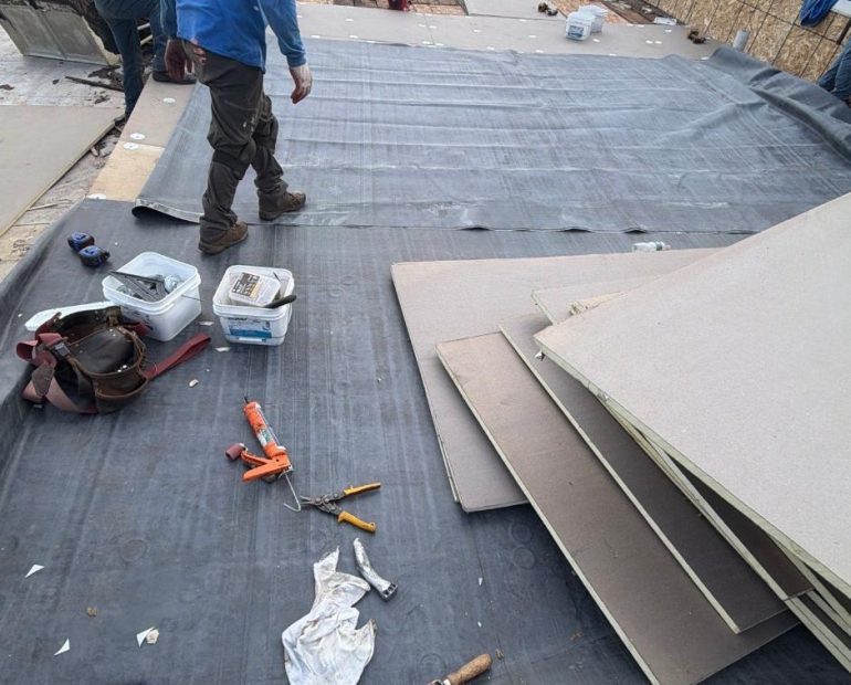 Commercial flat roof membrane preparation with workers installing roofing material over an exposed roof surface