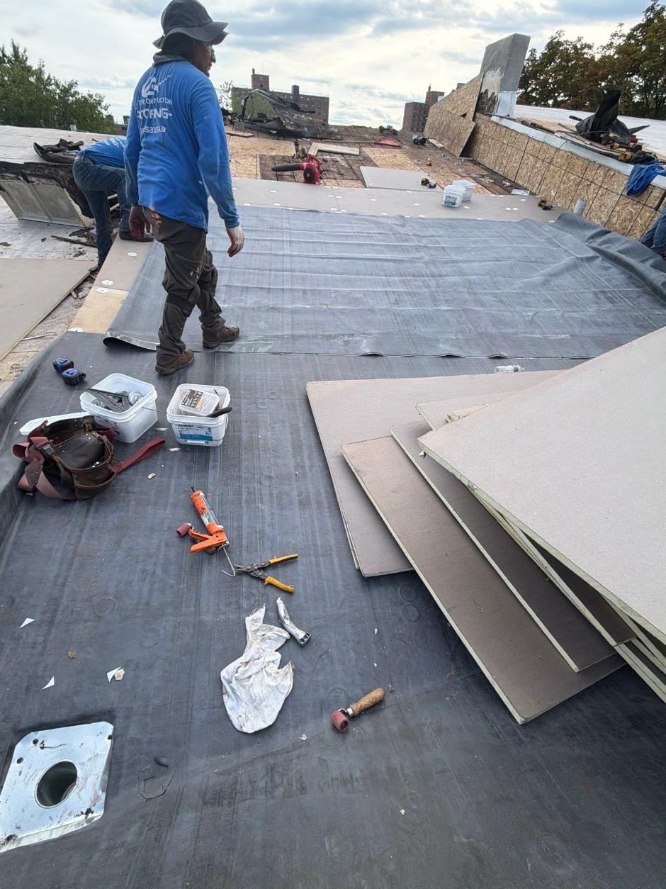 Commercial flat roof membrane preparation with workers installing roofing material over an exposed roof surface