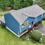 Aerial view of a blue two-story residential house with asphalt shingle roofing and a driveway