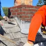 Roof replacement work near chimney showing damaged shingles and flashing