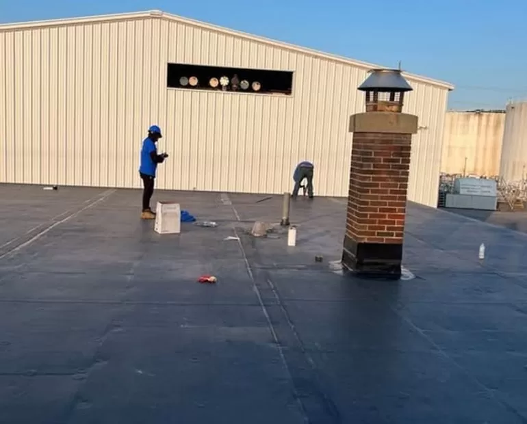 Professional roof leak repair on commercial flat roof with technicians sealing membrane and flashing