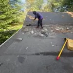 Worker removing old shingles during a residential roof replacement project to prepare for new roofing installation