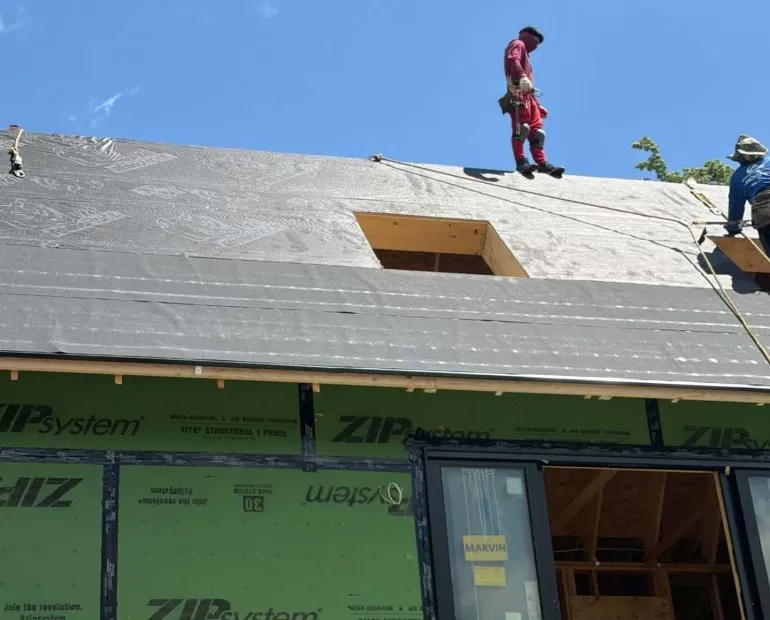 Synthetic Roofing Underlayment vs Felt: Which Is Better for Your Roof? synthetic roofing underlayment vs felt Professional roofers installing synthetic roofing underlayment over ZIP System roof sheathing before asphalt shingles on a new residential home.