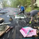 Professional roofers installing synthetic underlayment before asphalt shingles during a residential roof replacement.