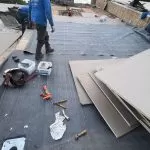 Commercial flat roof membrane preparation with workers installing roofing material over an exposed roof surface