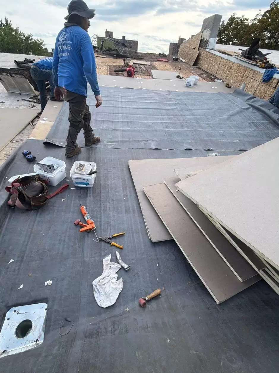 Commercial flat roof membrane preparation with workers installing roofing material over an exposed roof surface